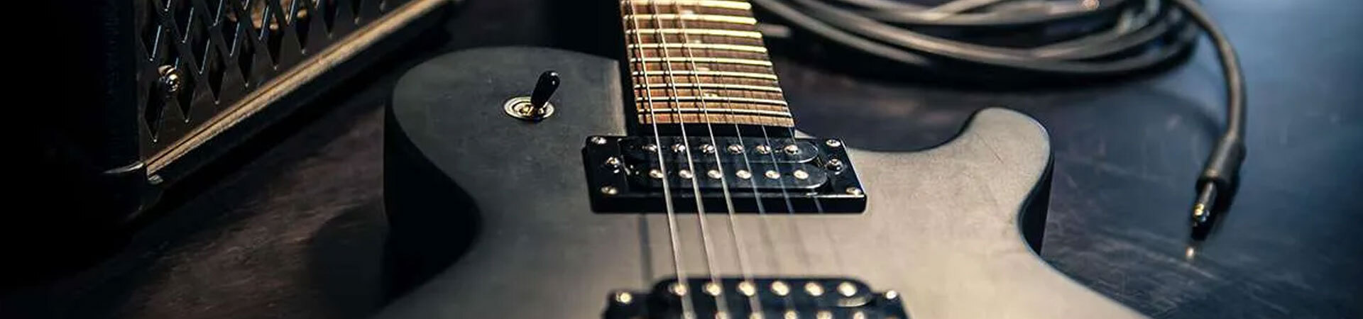 A close up of a moody looking black guitar on a dark wooden floor near an amp